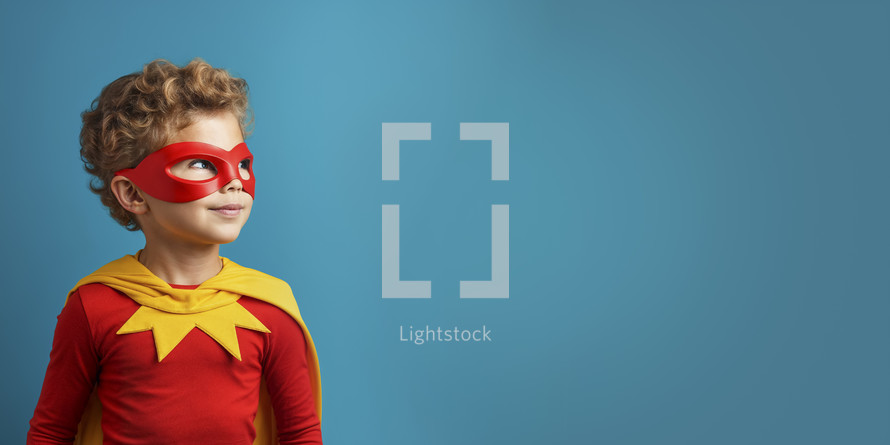 Cheerful young boy in red superhero costume with mask, looking up with inspiration against a teal background.