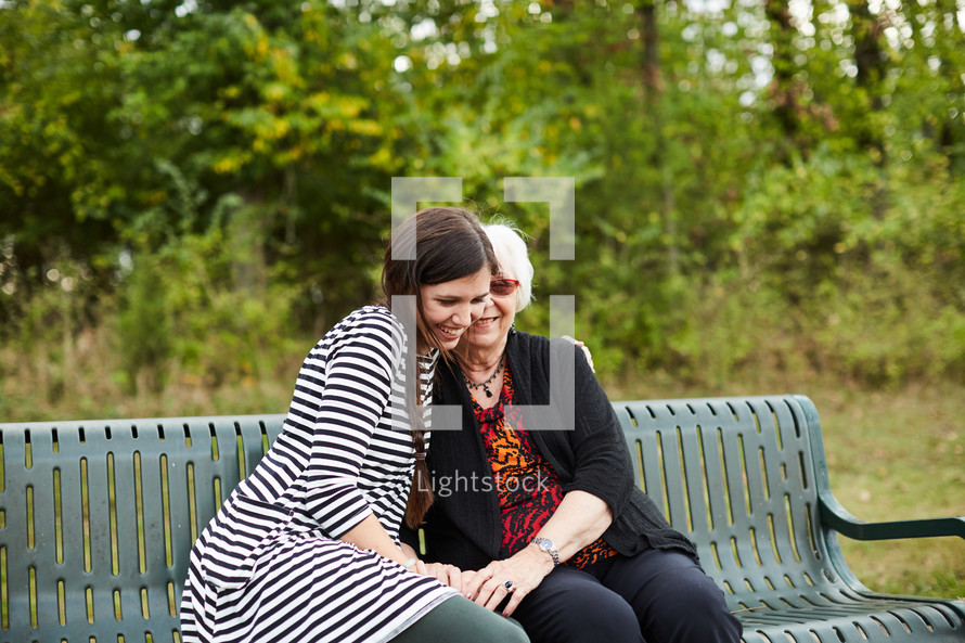 elderly woman praying with a young woman on a park bench 