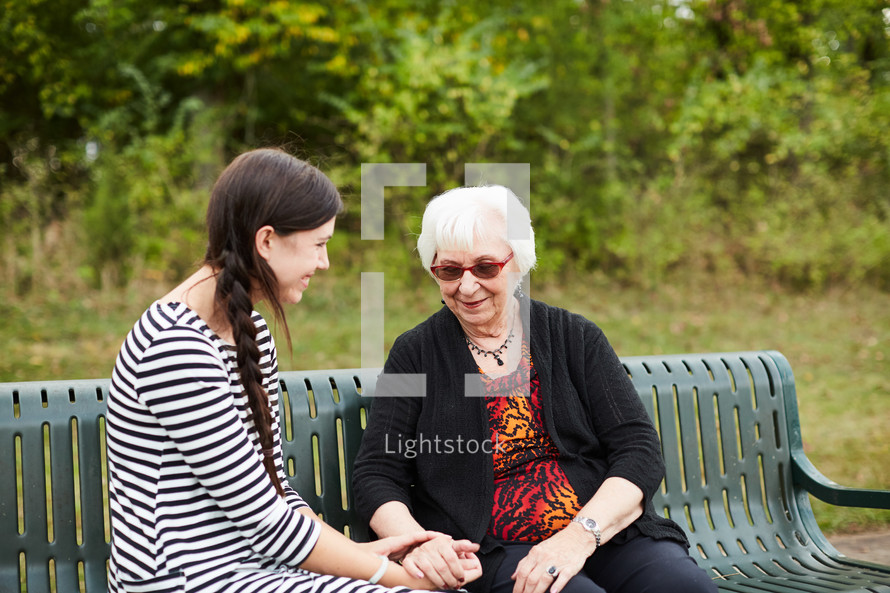 Mature woman laughing and talking with a young woman on a park bench 
