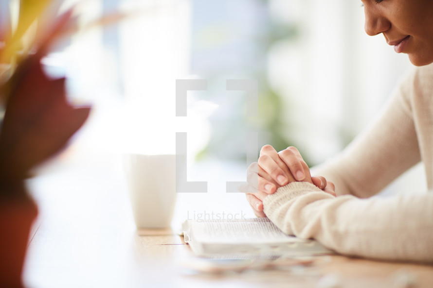 woman sitting at a desk praying over a Bible 