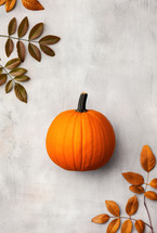 Minimalist autumn composition featuring a bright orange pumpkin and fall leaves on a light background, ideal for Thanksgiving decor.