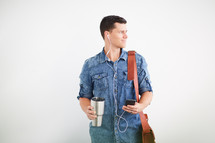 a man standing holding a messenger bag listening to earbuds 