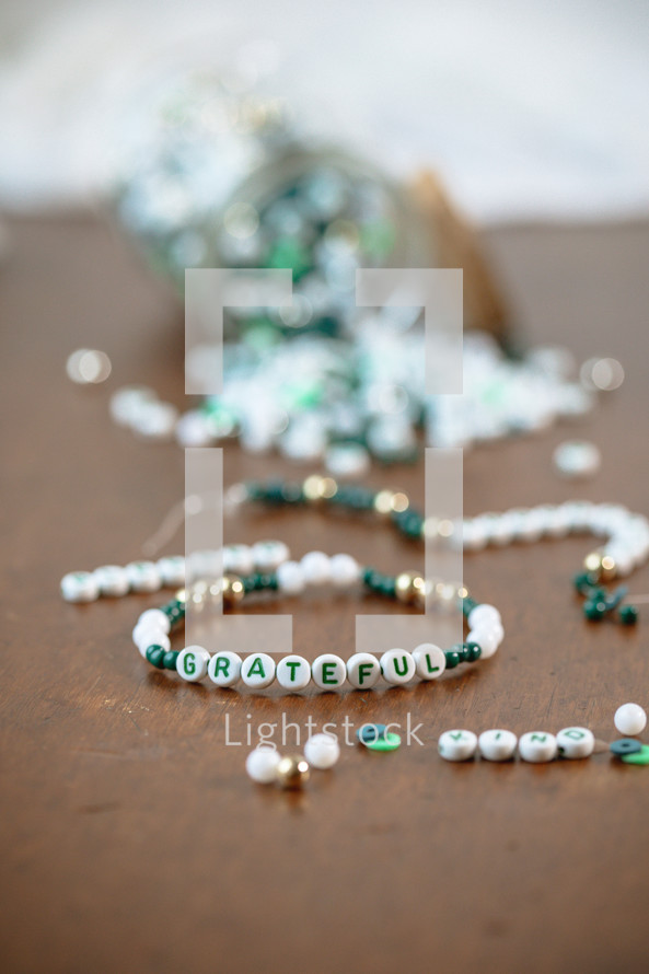 Jar of green, white, and gold beads with word - grateful