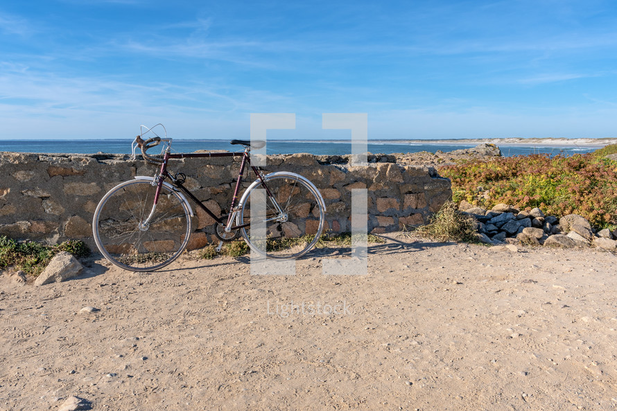 bike leaning against a stone wall on a beach 