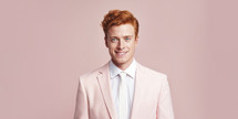 Stylish young man with ginger hair in a pastel pink suit against a pink background.