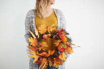 a woman standing holding a fall wreath 