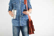 a man standing holding a messenger bag listening to earbuds 