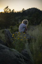 a little girl sitting outdoors in a field in summer 