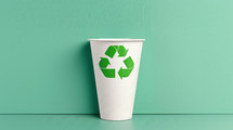 White paper cup with a green recycling symbol, placed against a light green background, emphasizing eco-friendly practices and recycling.