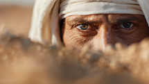 A close-up of a man's intense eyes peering through a desert environment, depicting a biblical spy in Jericho, conveying themes of secrecy and vigilance in an ancient context.