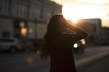 a woman walking down a sidewalk at sunset tucking her hair behind her ear 