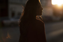 a woman walking down a sidewalk at sunset looking back at the camera 