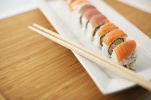 A sushi roll and chopsticks on a white plate.