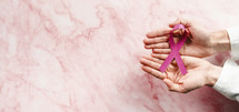 Hand holding ribbon on a flat layer marble table for world cancer awareness day
