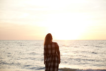 a woman standing on a shore looking out at the ocean 