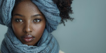 Portrait of a young woman with a serene expression, wrapped in a soft denim-textured scarf, set against a pale blue backdrop.