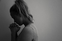 A young woman with hands clasped and head bowed in prayer.
