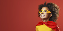 Joyful young Afro-European girl in superhero costume with mask and cape, looking up with a hopeful smile, against a red background.