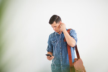 a man standing holding a messenger bag listening to earbuds
