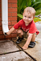 toddler boy playing with a rain spout 