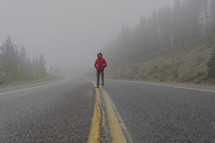 man standing in the middle of a road in fog 
