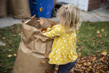 Little girl helping bag up fall leaves