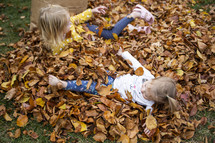 Little girls playing in a pile of fall leaves