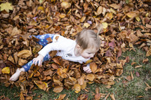 Little girl playing in a pile of fall leaves