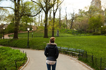 a woman walking on a path through a park 