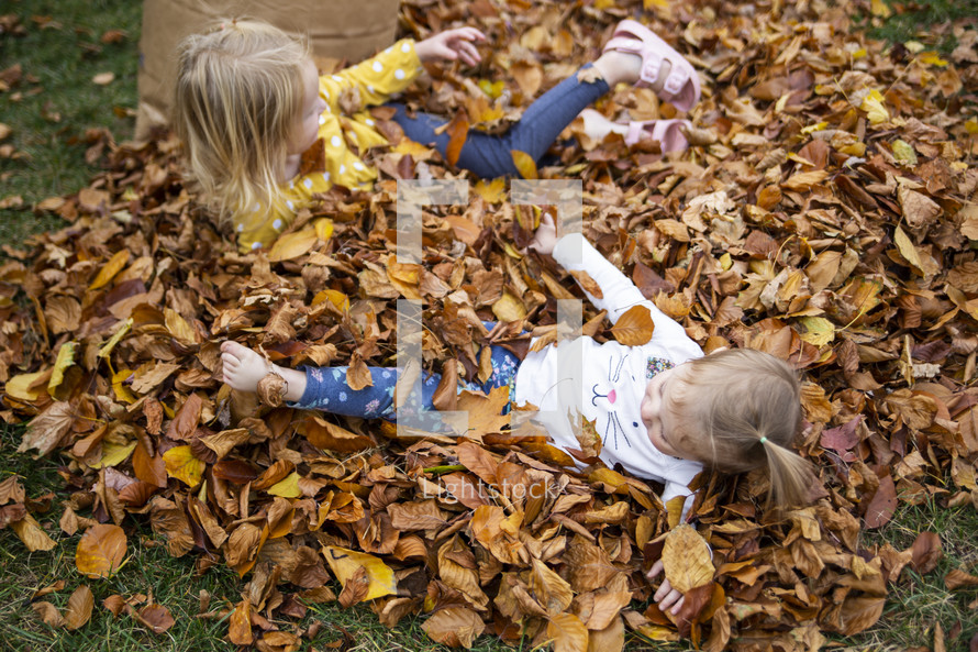Little girls playing in a pile of fall leaves