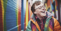 Joyful young man with Down syndrome in colorful winter clothing, vibrant mural backdrop.
