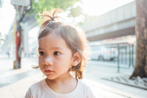 face of a little girl standing on a sidewalk 