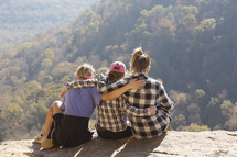 friends embracing sitting with legs hanging over a cliff 