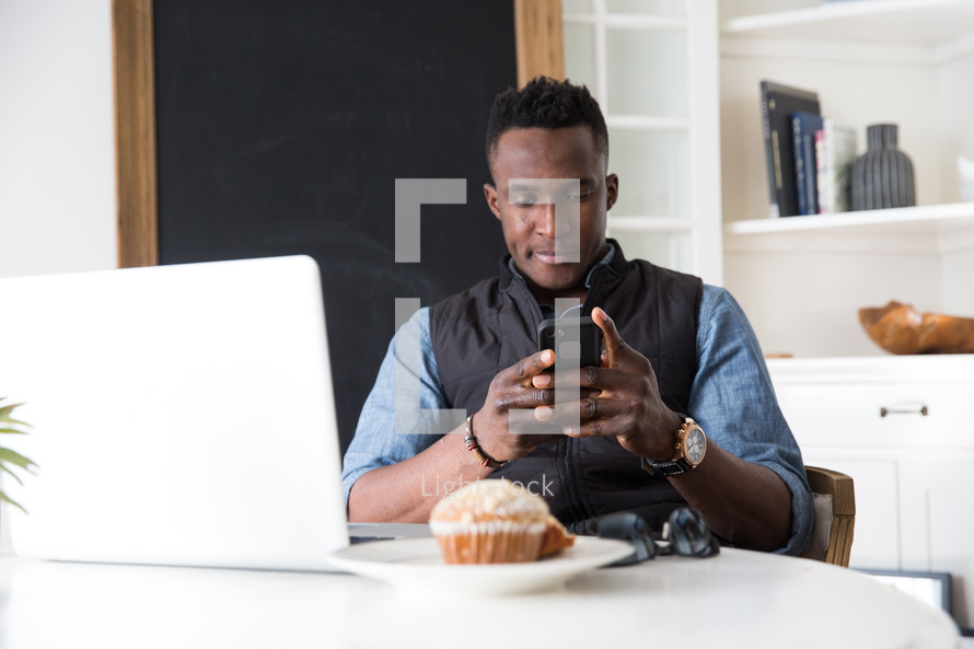 man in front of a laptop checking his cellphone 
