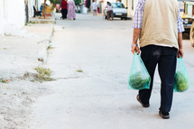 a man walking carrying bags of watermelons 
