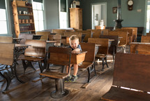 a toddler boy sitting in a desk of an old school house 