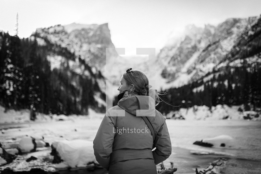 Female Hiker enjoying snowfall beside a lake in the mountains