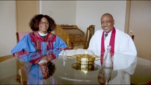 Pastors sitting at a table smiling with Bible and communion tray