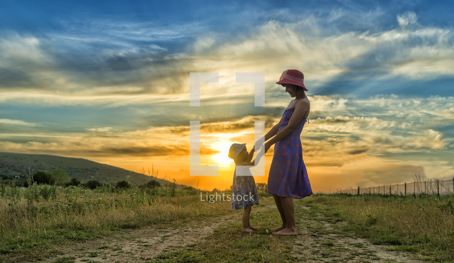mother and child standing barefoot on a dirt road in summer 