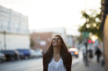 a woman walking down a sidewalk happily looking up.