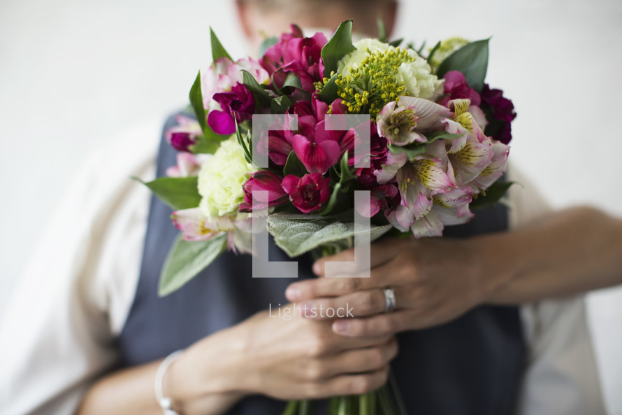 Woman's hands holding a bouquet of flowers behind a man's back.
