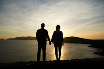silhouette of a couple holding hands by a shore 