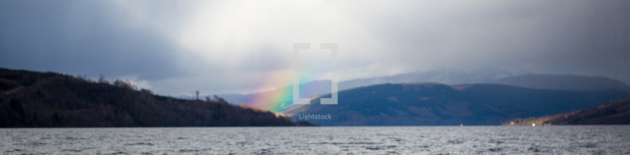 a rainbow between mountains near a lake 