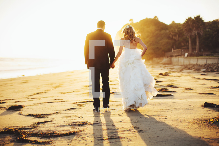 bride and groom walking holding hands on a beach