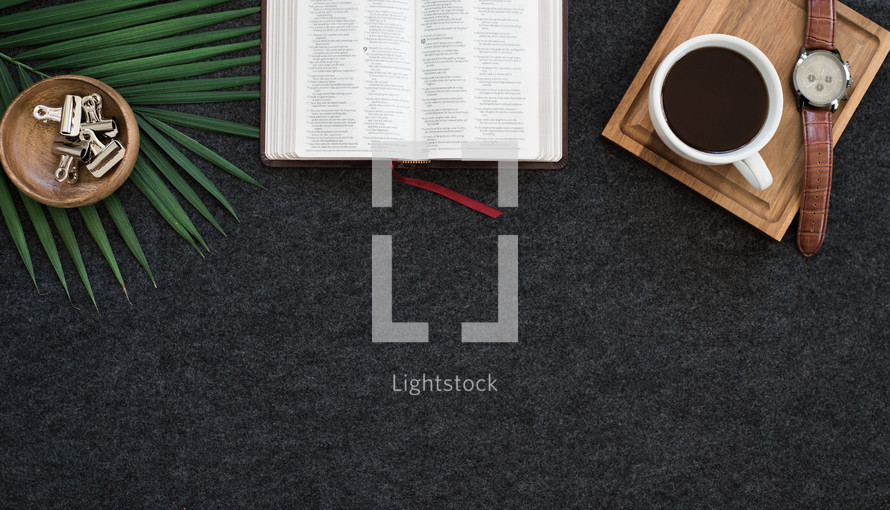 open Bible, palm fronds, watch, and coffee on a desk 