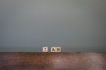 Wooden tiles spelling "I Am" on wooden table
