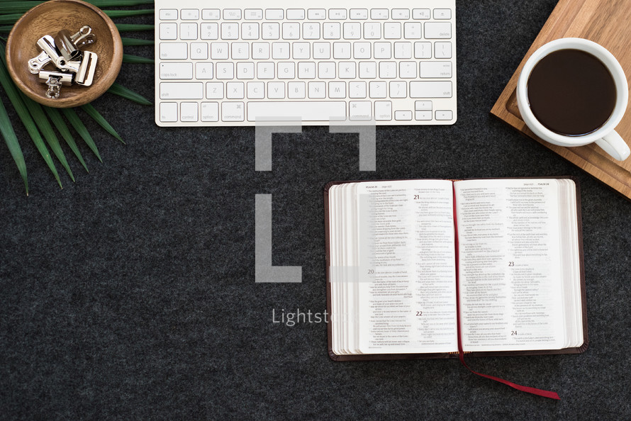 keyboard, open Bible, bowl, clips, and coffee on a desk 