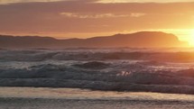 waves washing onto a shore at sunset 