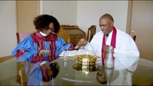 Pastors sitting at a table holding hands and praying with Bible, oil and communion tray on the table   