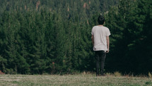 man standing in a field looking out at a forest 